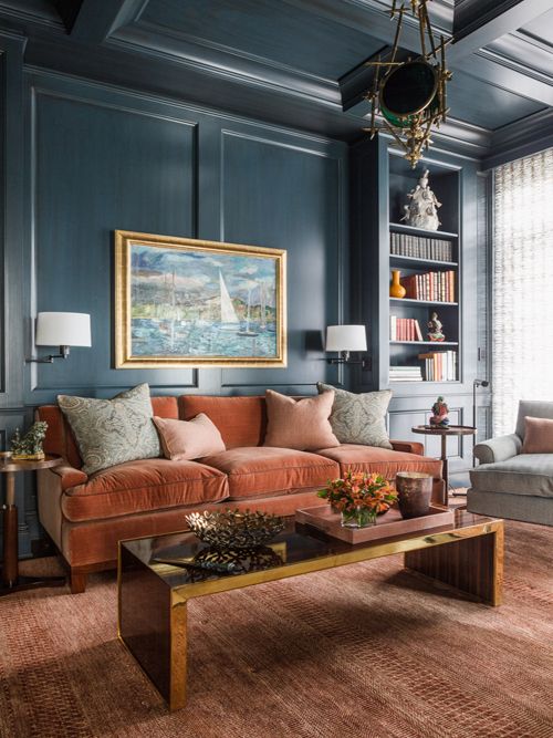 a sophisticated living room with navy walls, a rust-colored velvet sofa, a low polished table, built-in shelves