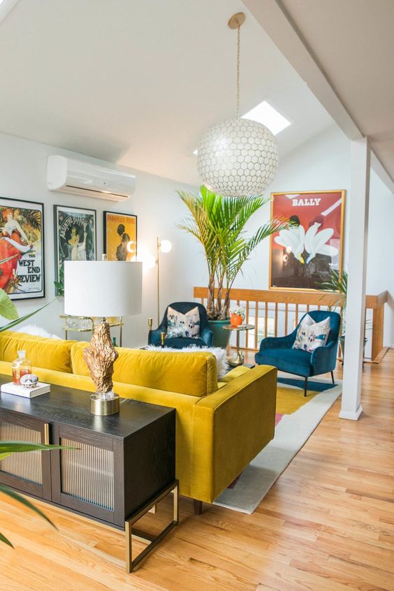 a vibrant mid-century modern space with a yellow sofa and blue chairs, floral pillows, potted plants and a credenza with a lamp