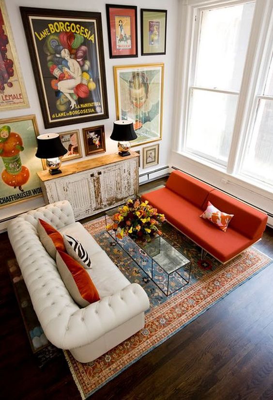 a whimsical living room with a bold gallery wall, a white tufted sofa, an orange sofa, a glass table and a shabby chic cabinet