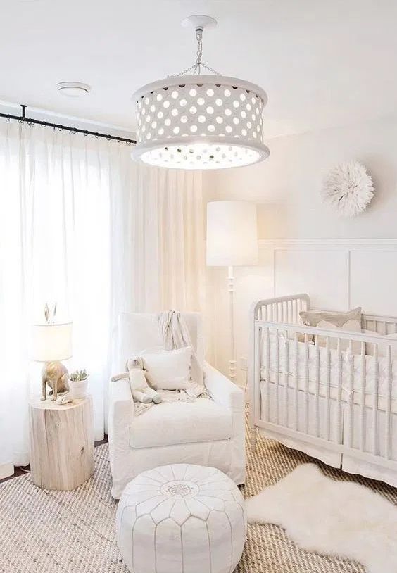 a white nursery with paneling, a crib, a chair, a leather pouf, a tree sutmp and a pendant lamp on chain