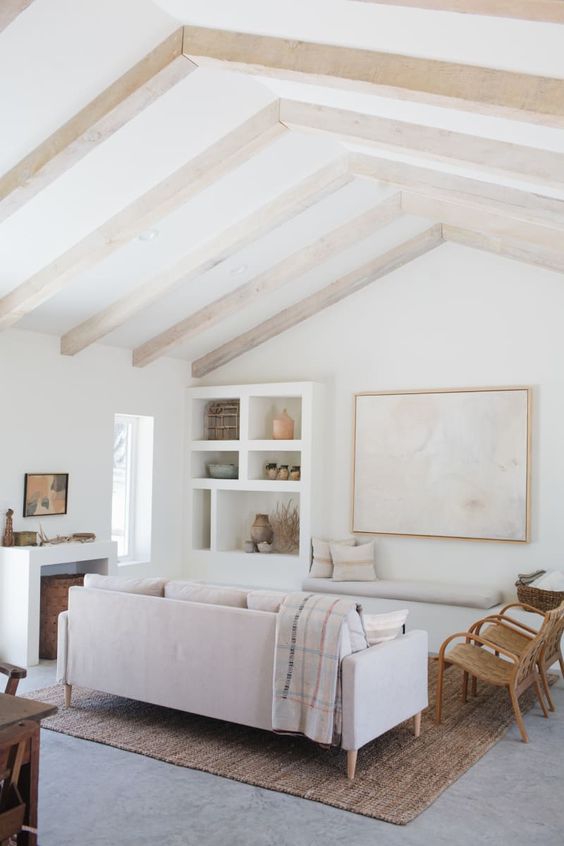an airy living room with blonde wood beams, neutral furniture and built-in shelves, printed textiles and a niche with a basket