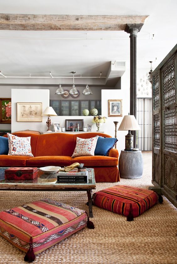 an eclectic living room with a burnt orange sofa, a low table and pretty tassel cushions and a table lamp