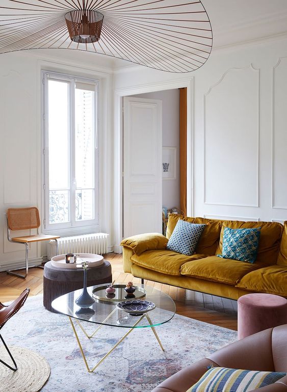 an exquisite Parisian living room with a mustard sofa, blush and brown chairs, a low glass table and a beautiful chandelier