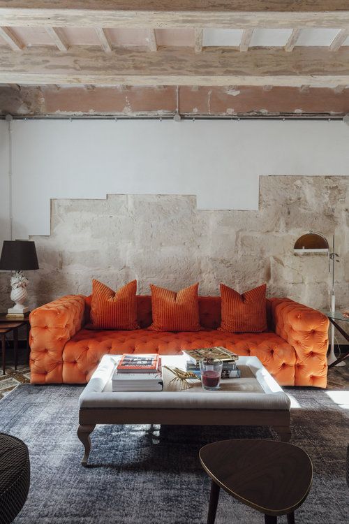 an industrial living room with rough walls, a refined orange tufted sofa, a low glass table and floor lamps