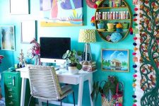 a boho maximalist home office with a turquoise accent wall, a white desk, a green cabinet and lots of artworks and textiles in bold shades