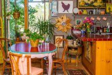 a boho maximalist kitchen with grey walls, light stained cabinets, a red tile countertop, a red table and mismatching chairs, lots of art and boho rugs