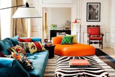 a bold living room with a turquoise sofa, colorful pillows, an orange daybed, an animal print ottoman, a striped rug and a red refined chair
