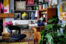 a bold maximalist home office with a blue wall, a fireplace, a vintage bureau desk, colorful artworks and potted plants