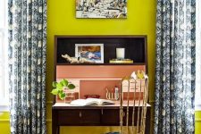 a bright home office with neon yellow walls, a vintage dark stained desk, a gilded chair with a tropical seat and printed curtains