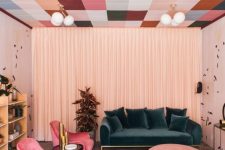 a bright living room with a printed colorful ceiling, a dark green sofa, bright pink chairs and light pink ottomans