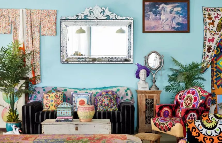 a bright maximalist living room with blue walls, colorful furniture, bright pillows and bold curtains is a crazy and very eclectic space