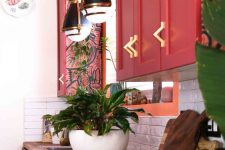 a chic maximalist kitchen with red cabinetry, butcherblock countertops, retro pendant lamps and lots of potted plants