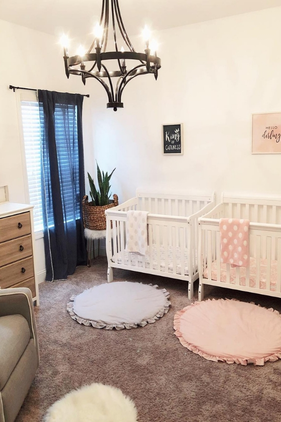 a chic nursery with white walls and white and grey furniture, layered rugs, a metal chandelier, a navy curtain and some potted plants