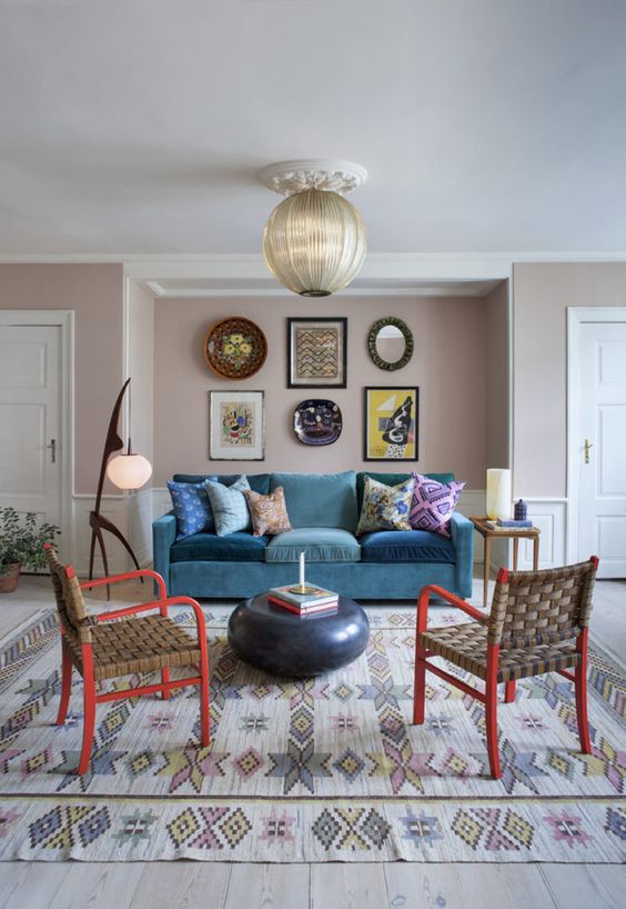 a colorful living room with blush walls, a turquoise sofa, red chairs, a bright gallery wall and catchy lamps