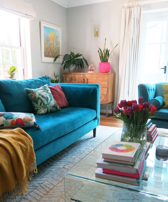 https://www.digsdigs.com/photos/2021/05/a-colorful-living-room-with-dove-grey-walls-a-turquoise-sofa-bright-pillows-and-accessories-an-acrylic-coffee-table-and-bold-blooms.jpg