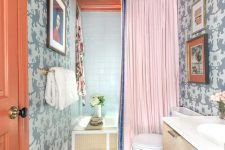 a colorful maximalist bathroom with grey printed walls, a rust ceiling and a door, a bold rug, a creative agate chandelier and a pink curtain