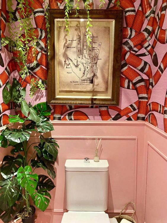 a colorful maximalist bathroom with pink paneling, snake print wallpaper,  potted plants and a bold artwork is creative