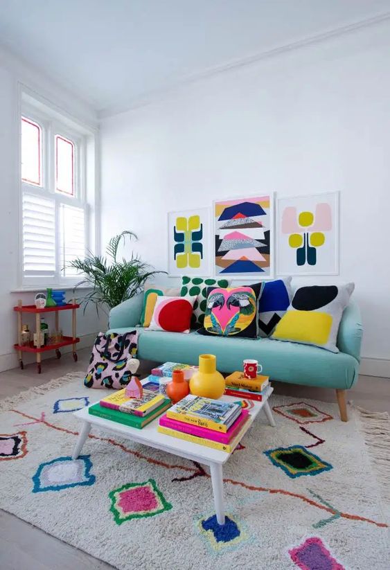 a colorful retro-inspired living room with a turquoise sofa, a colorful rug, a gallery wall, pillows and books fill the space with bright colors