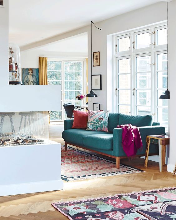 a contemporary living room with a fireplace, a turquoise sofa and bright textiles, pendant lamps and printed mini rugs
