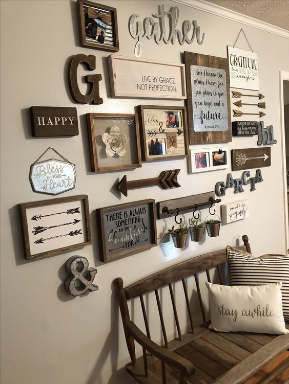 a cool vintage rustic gallery wall with arrows, monograms, various artworks and signs in frames, greenery in buckets