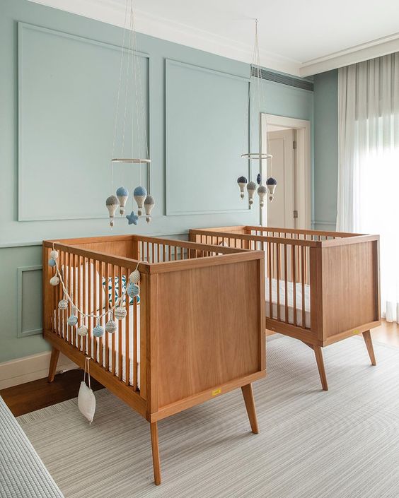 a dreamy twin nursery with blue paneled walls, lovely stained cribs, mobiles and neutral textiles is a very welcoming space