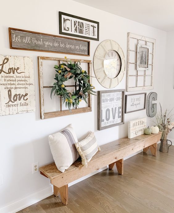 a farmhouse gallery wall with a clock in a thick frame, a window frame with a wreath, some plaques and metal monograms is cute