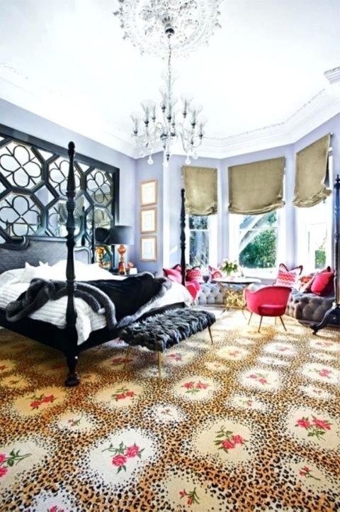 a gorgeous maximalist bedroom with lilac walls, a black bed and an ottoman, red chairs and a grey windowsill bench, a crystal chandelier