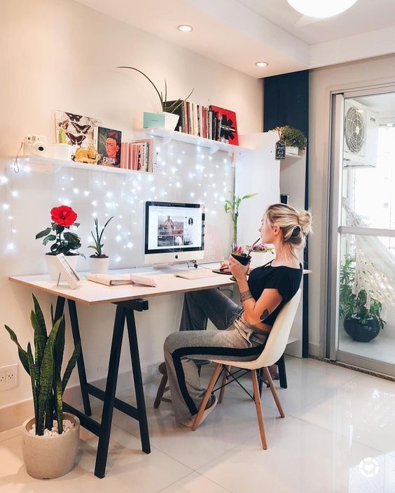 a lovely home office with a trestle desk, a white chair, open shelves and a storage unit, potted plants and lights hanging down