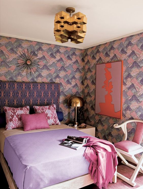 a lovely maximalist bedroom with brushstroke walls, a printed bed, pastel bedding, a pink chair, a gold sculptural chandelier