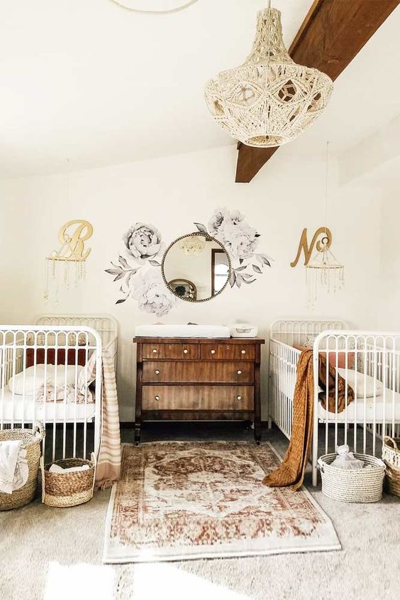 a lovely nursery with a wooden beam on the ceiling, white cribs, a stained dresser, a boho rug and textiles plus baskets for storage