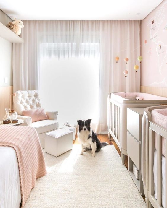 a lovely twin nursery with blush walls, grey cribs, a creamy chair with a footrest and a daybed, blush textiles and pretty mobiles