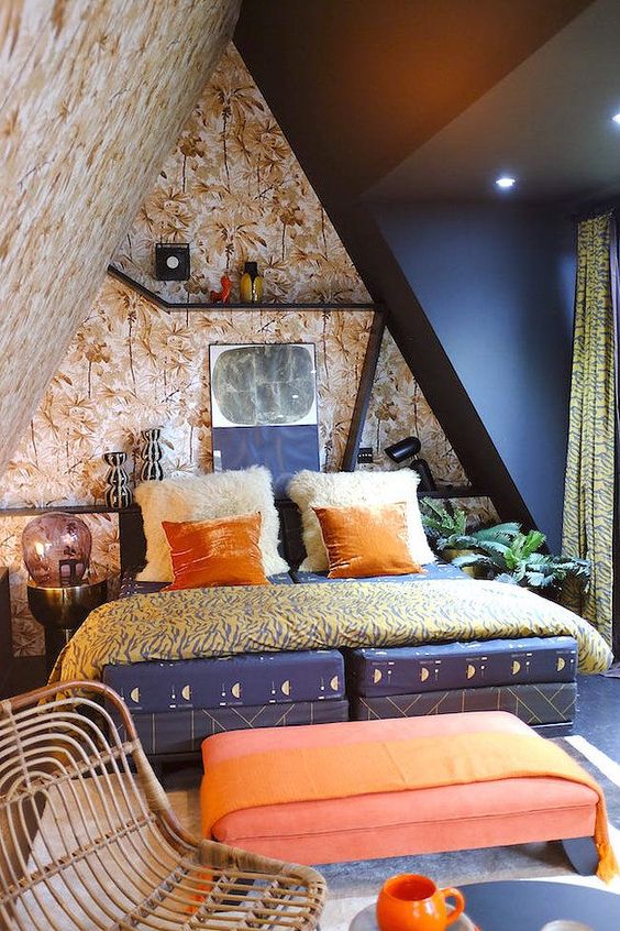 a maximalist attic bedroom with botanical walls and a black one, a navy bed, a coral ottoman, bright bedding and shelves