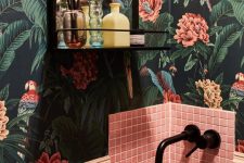 a maximalist bathroom with dakr floral wallpaper, pink tiles, a pink sink, black fixtures and a black shelf
