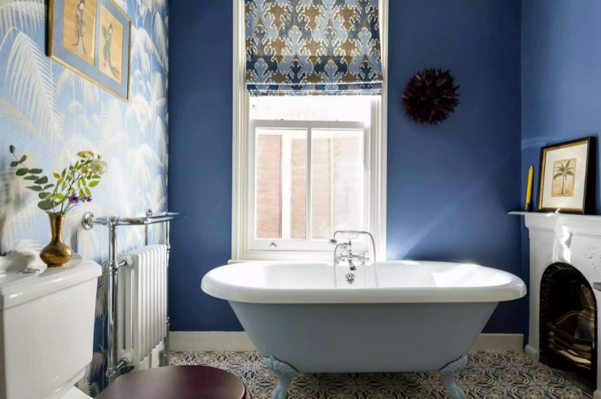 a maximalist bathroom with navy walls and an accent tropical one, a fireplace and a blue tub, a printed curtain and a stained stool