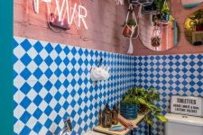 a maximalist bathroom with pink brick walls, blue and white checked tiles, a console table, potted greenery, a neon sign and mirrors