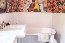 a maximalist bathroom with white paneling and bold printed wallpaper, blue tiles on the floor, with artworks and a dog