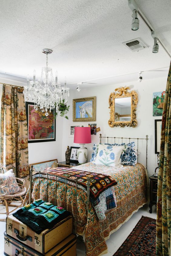 a maximalist guest bedroom with a metal bed, a rattan chair, vintage nightstands, floral textiles and a gallery wall