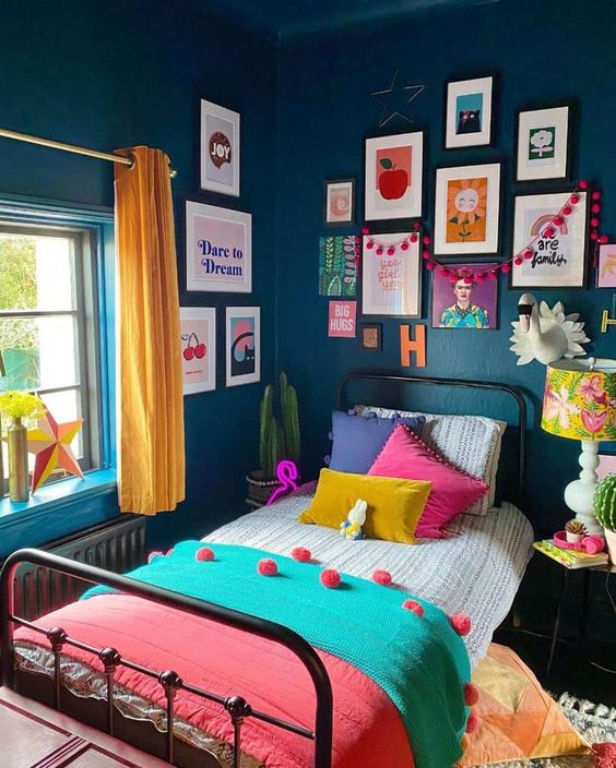 a maximalist guest bedroom with a metal bed, navy walls, a colorful gallery wall, a bright floral lamp and yellow curtains, colorful bedding