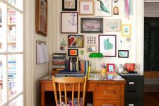 a maximalist home office wiht a vintage desk and chair, a colorful gallery wall and bold books and a table lamp