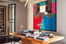 a maximalist home office with a large shared desk, colorful books, a bold statement artwork, printed chairs and a sunburst lamp