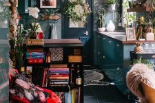 a maximalist kitchen with dark and tropical leaf walls, blue cabinets and a black kitchen island, a red chair and potted plants