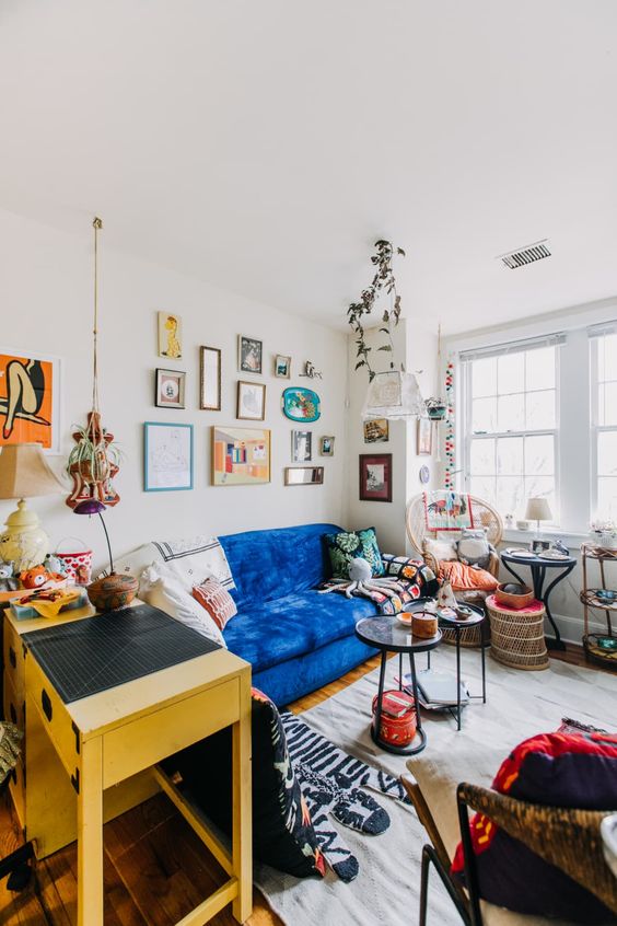 a maximalist living room with a bold blue sofa, a yellow console table, a bright gallery wall, a rattan chair and round tables