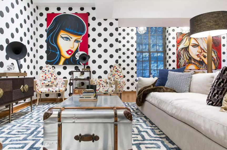 a maximalist living room with a neutral sofa, a metal suitcase as a table, polka dot chairs of quirky shapes, polka dot wlals and pop art pieces