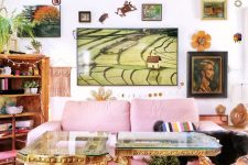 a maximalist living room with a pink sofa, a refined double table with glass tabletops, a bold and creative gallery wall and a bookcase with plants