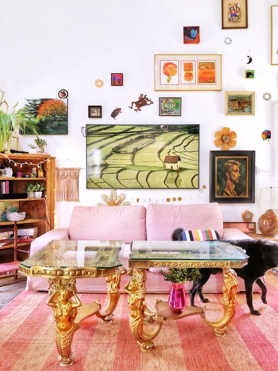 a maximalist living room with a pink sofa, a refined double table with glass tabletops, a bold and creative gallery wall and a bookcase with plants