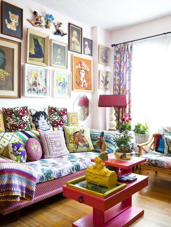 a maximalist living room with a pink sofa and a coffee table, a floral chair, a bright gallery wall and potted plants and blooms