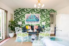 a maximalist living room with a tropical accnet wall, a grey sofa and neon chairs, a statement plant and a chandelier