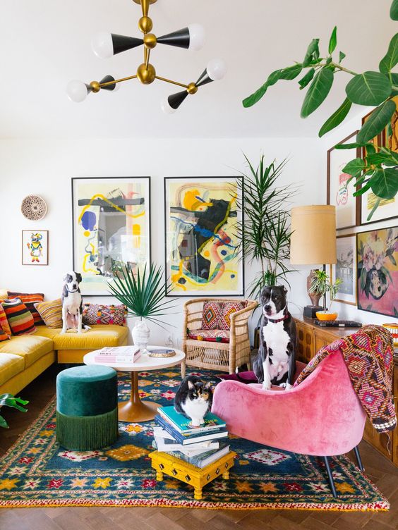 a maximalist living room with a yellow sofa, a pink chair, a colorful rug, a colorful gallery wall and statement plants