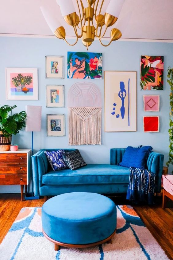 a maximalist living room with blue walls, a bold gallery wall, a bold blue sofa and an ottoman, a colorful gallery wall and a cool chandelier