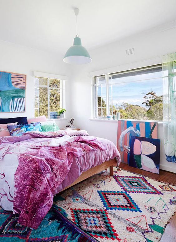 a maximalist ocean bedroom with simple furniture, colorful bedding and a bold artwork plus a gorgeous view